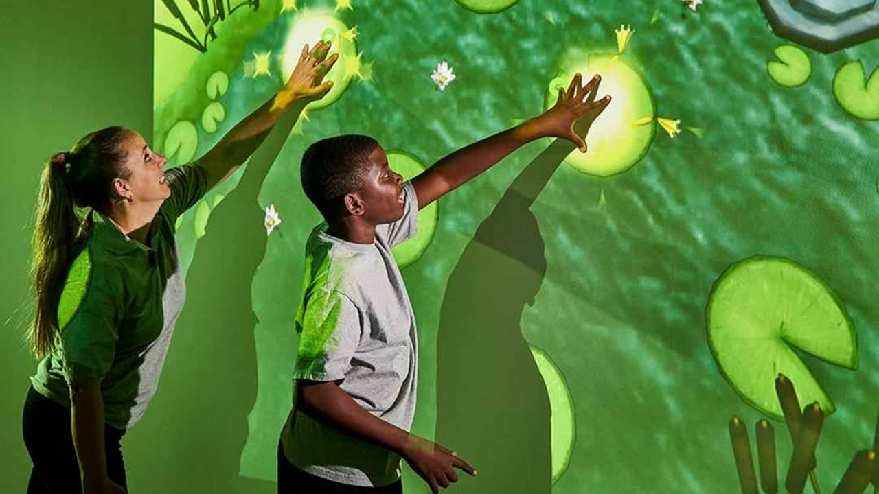 Niño y monitora tocando un muro interactivo con proyección de nenúfares